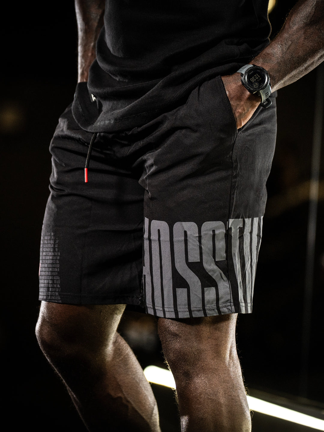 Person wearing black athletic shorts with Hosstile branding on a dark background#color_black