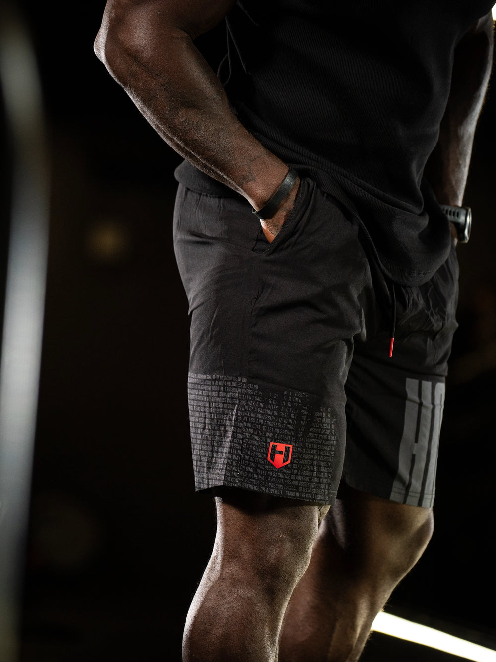 Person wearing black athletic shorts with a logo on a dark background#color_black