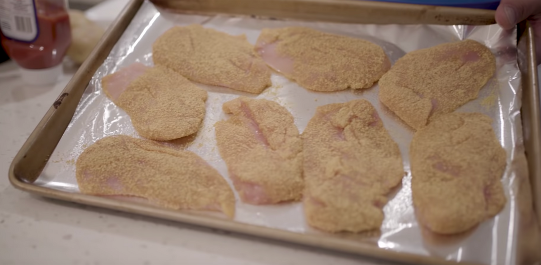 Chicken breast coated with shake-n-bake on a baking sheet