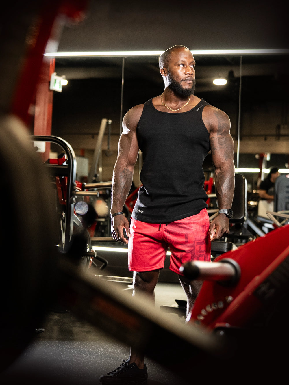 Man in a gym wearing a black tank top and red shorts#color_black