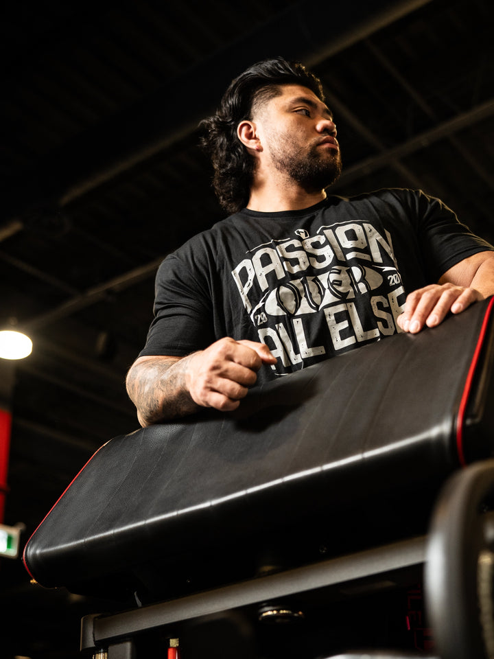 Man wearing a black t-shirt with text, standing next to a vehicle in an indoor setting#color_black