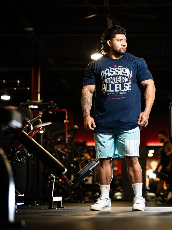 Man standing in a gym wearing a navy blue t-shirt with text and light blue shorts#color_navy