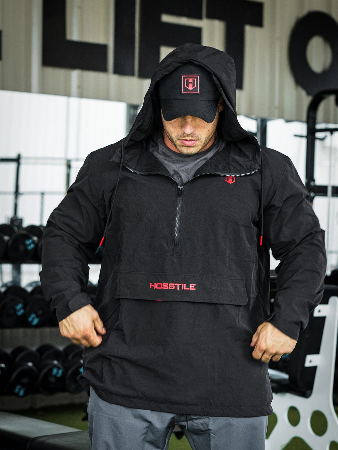 Bodybuilder Martin Fitzwater in a gym wearing a black hoodie windbreaker jacket and dark pants with visible branding#color_black