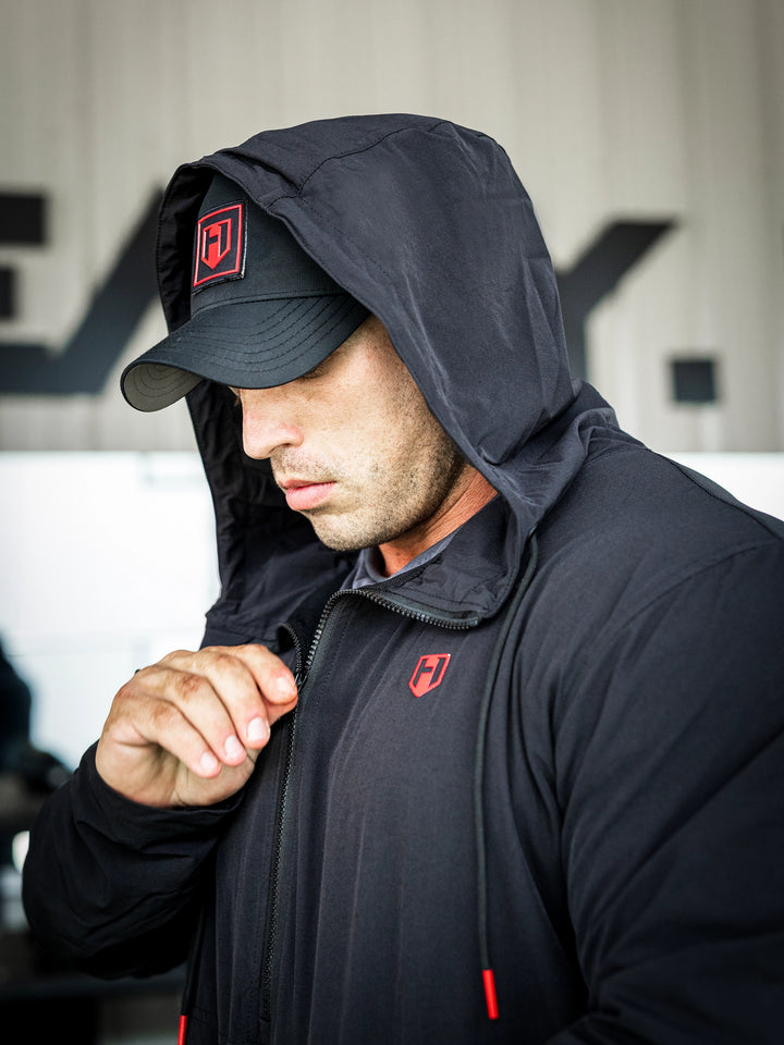 Bodybuilder Martin Fitzwater in a gym wearing a black hoodie windbreaker jacket and dark pants with visible branding#color_black
