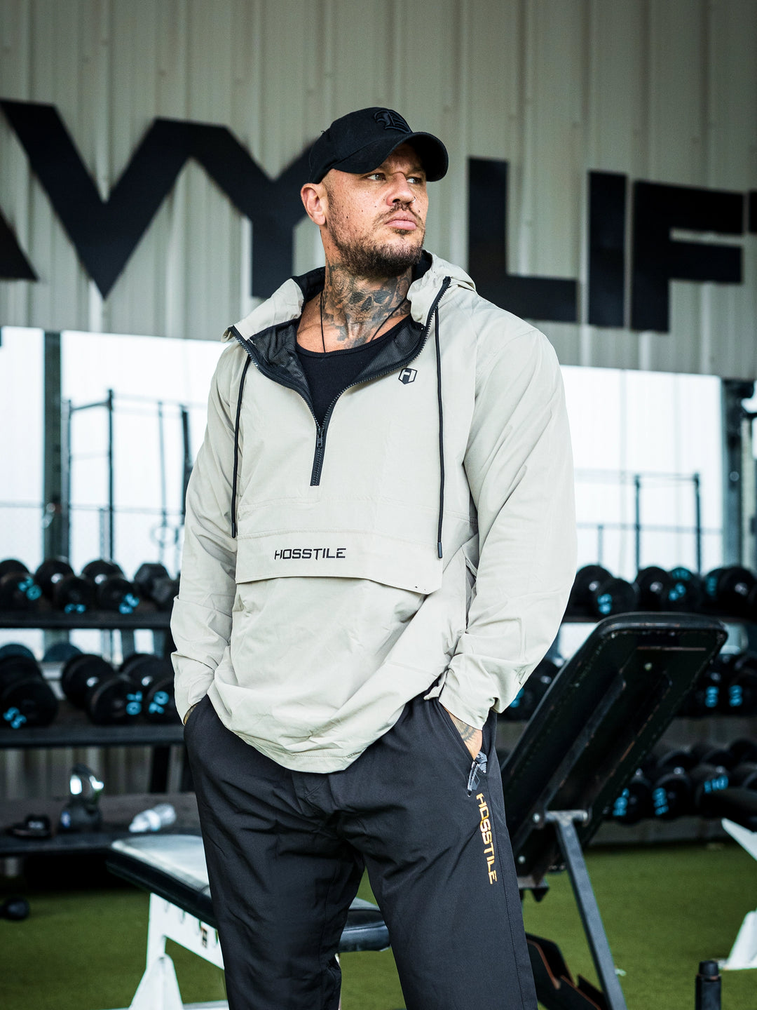 Bodybuilder Ben Chow in a gym wearing a light gray hoodie windbreaker jacket and dark pants with visible branding#color_cement