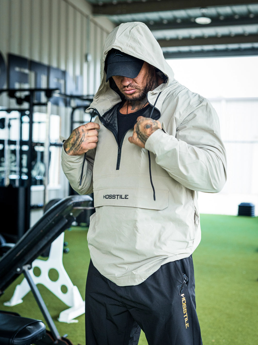 Bodybuilder Ben Chow in a gym wearing a light gray hoodie windbreaker jacket and dark pants with visible branding#color_cement