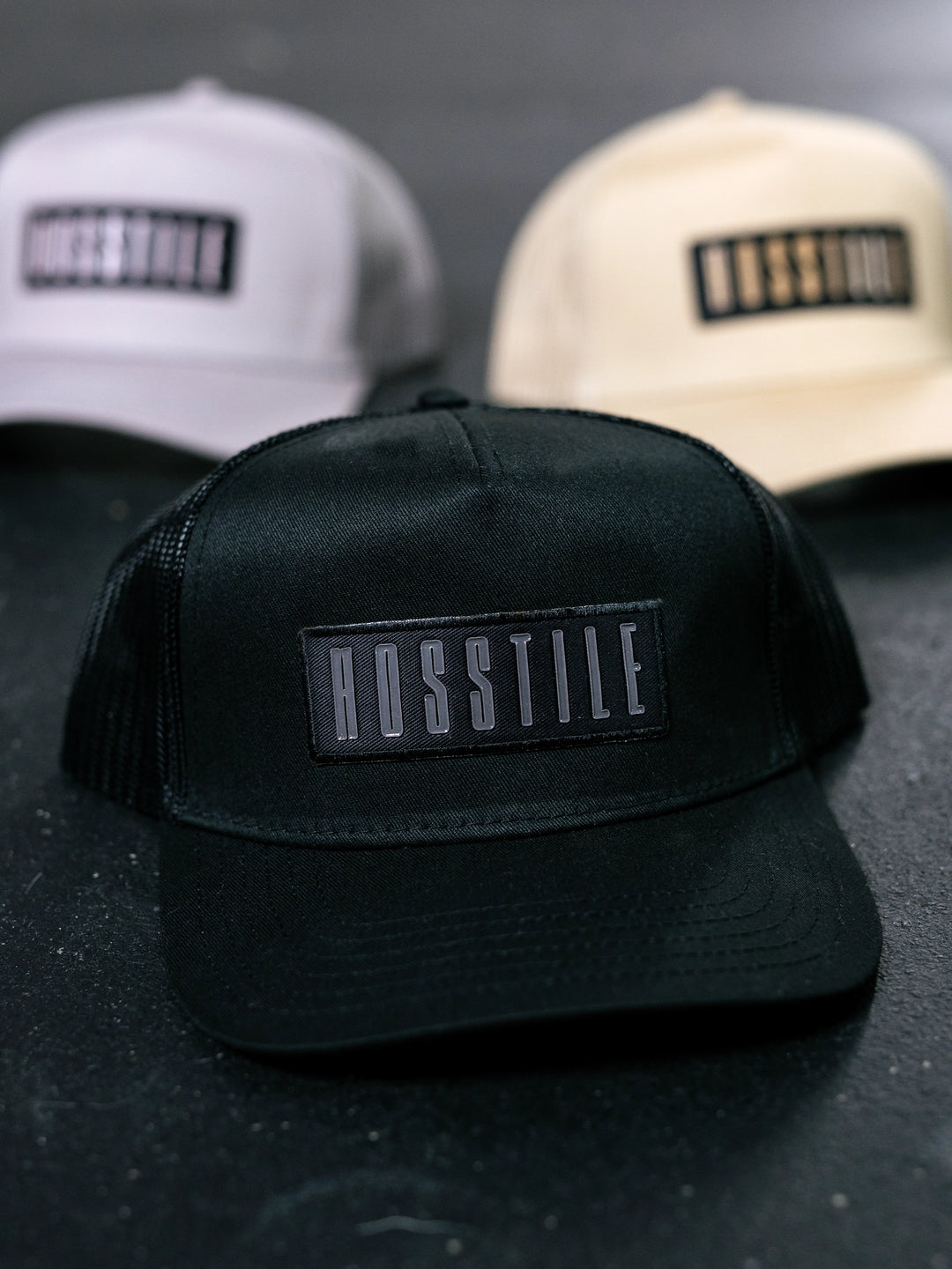 Black trucker hat with 'Hosstile' logo on a dark background.#color_black