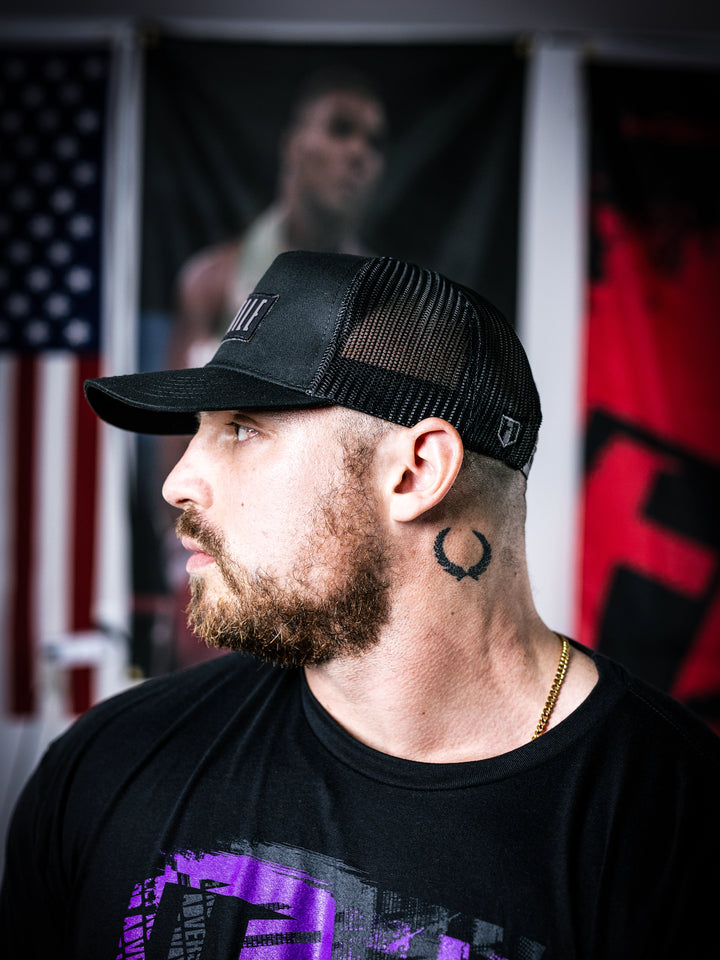 IFBB Martin Fitzwater wearing a black trucker hat with 'Hosstile' logo and a black t-shirt with graphic design.#color_black