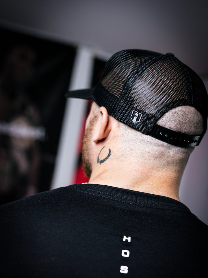 IFBB Martin Fitzwater wearing a black trucker hat with 'Hosstile' logo and a black t-shirt with graphic design.#color_black