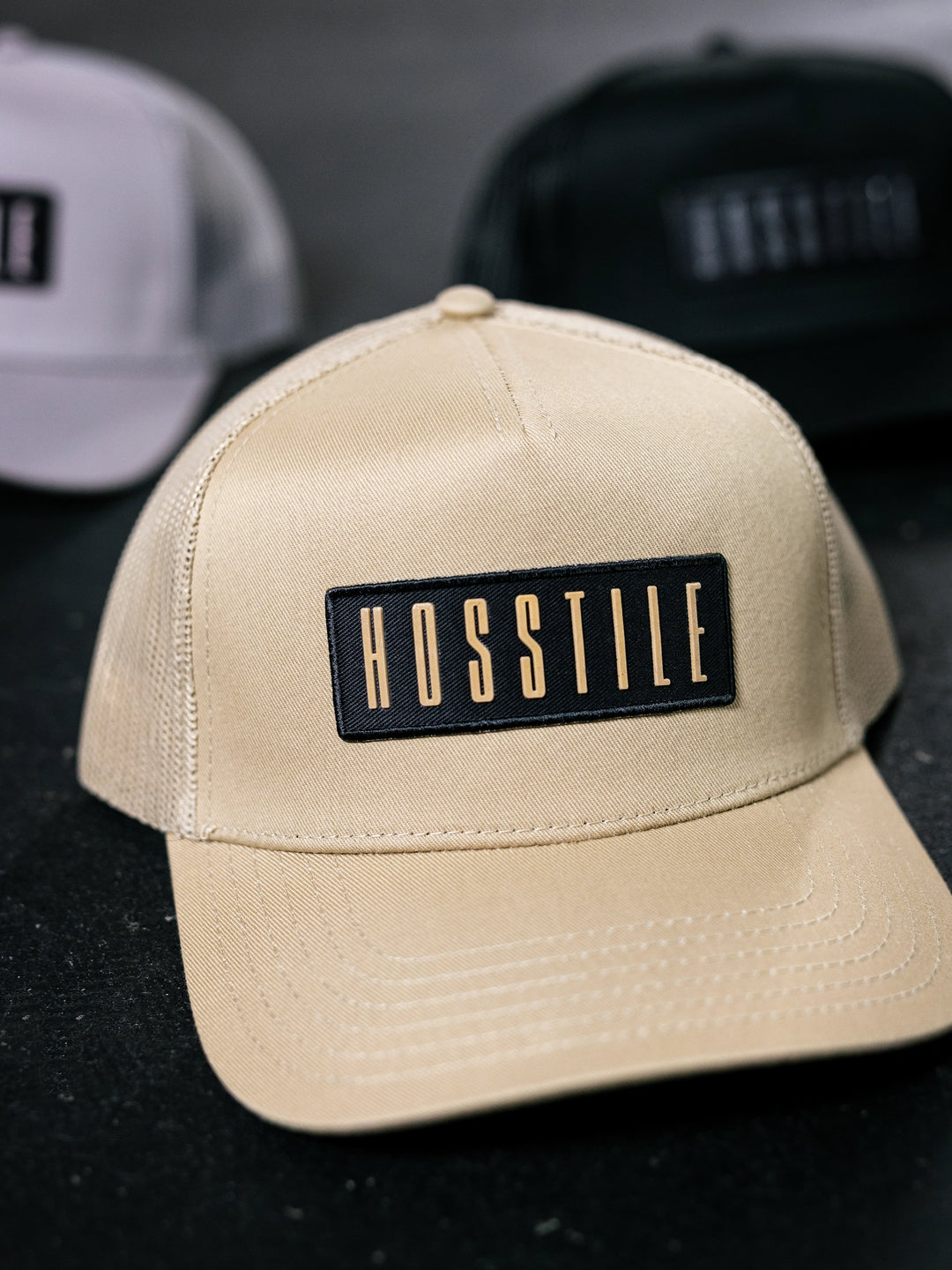 Beige cap with 'HOSSTILE' logo on a dark background.#color_desert-sand