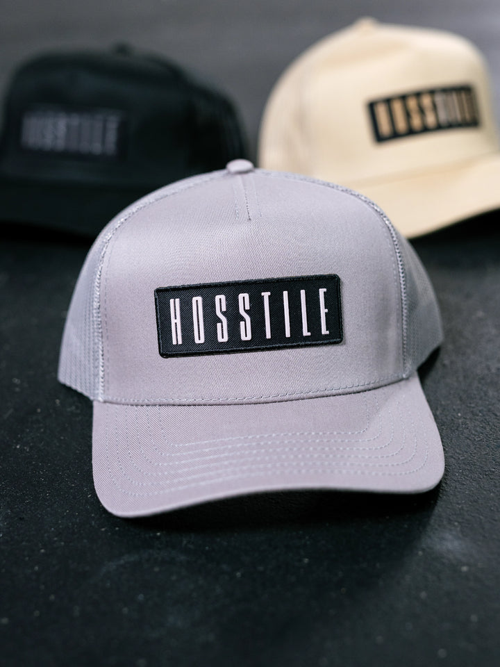 Gray cap with 'HOSSTILE' logo on a dark surface.#color_grey