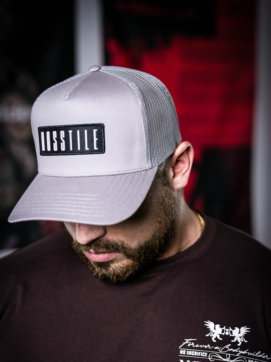 IFBB Martin Fitzwater wearing a grey trucker hat with 'Hosstile' logo and a  t-brown shirt with graphic design.#color_grey