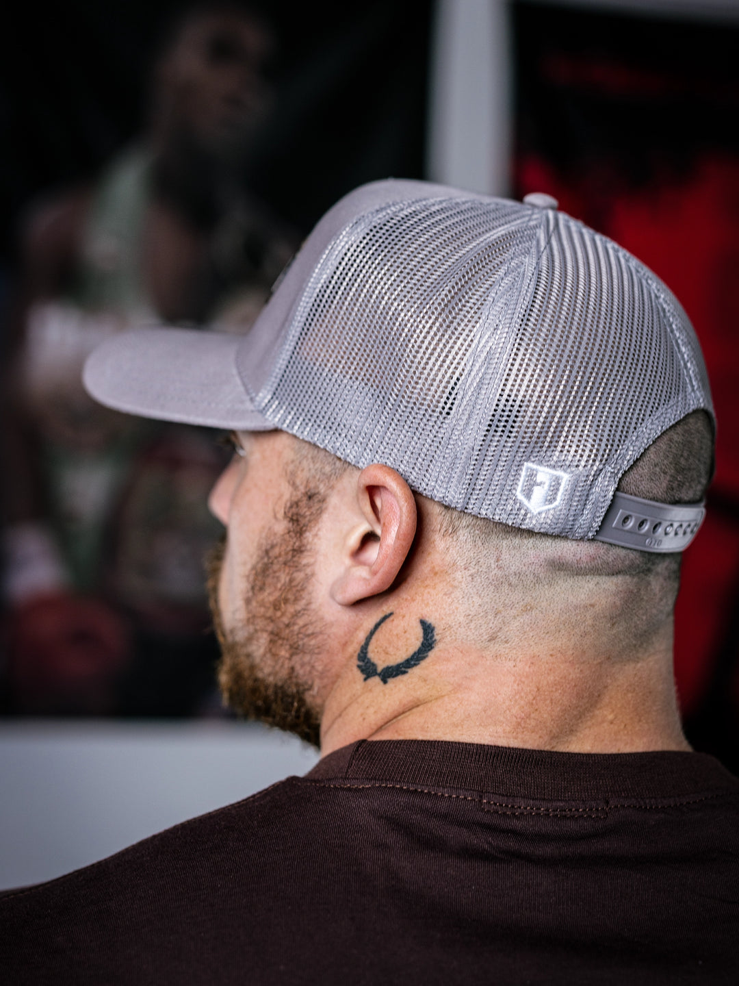 IFBB Martin Fitzwater wearing a grey trucker hat with 'Hosstile' logo and a  t-brown shirt with graphic design.#color_grey