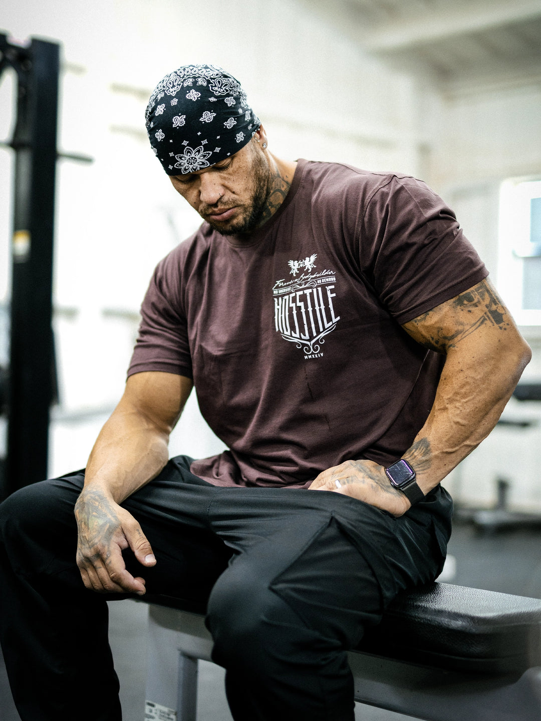 Bodybuilder Ben Chow sitting on a bench in a gym wearing a t-shirt with text and graphics.#color_mahogany