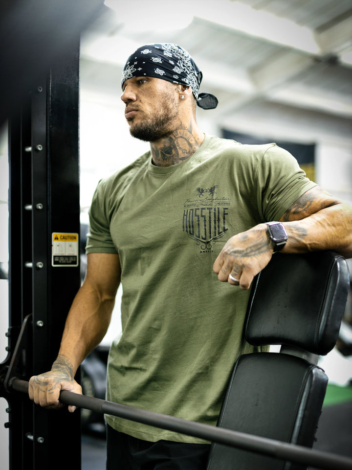 Bodybuilder Ben Chow standing in a gym wearing a t-shirt with text and graphics.#color_military-green