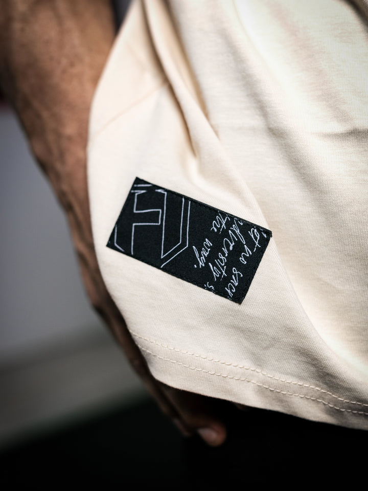 Close-up of a beige shirt with a black label featuring white text and design.#color_off-white