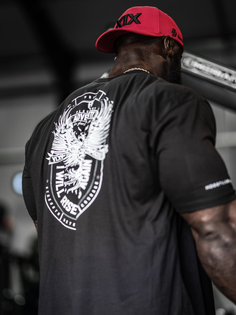 Samson Dauda wearing a black t-shirt with a white eagle design on the back, standing in an indoor setting#color_black