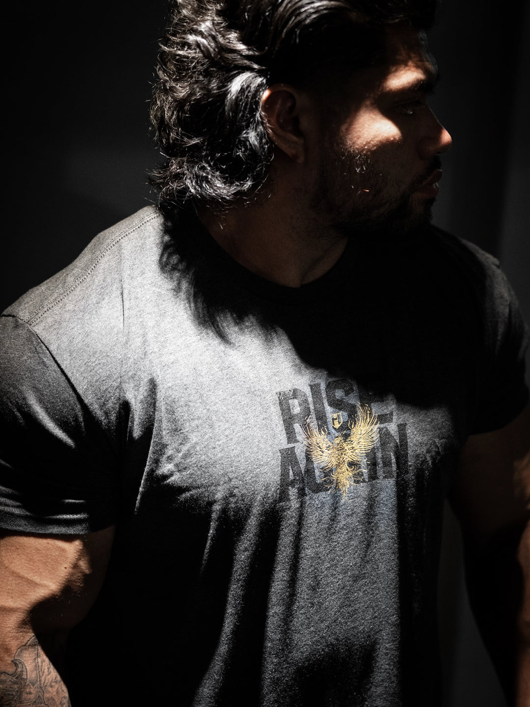 Man wearing a t-shirt with 'Rise Again' printed on it, standing in a dark setting#color_charcoal