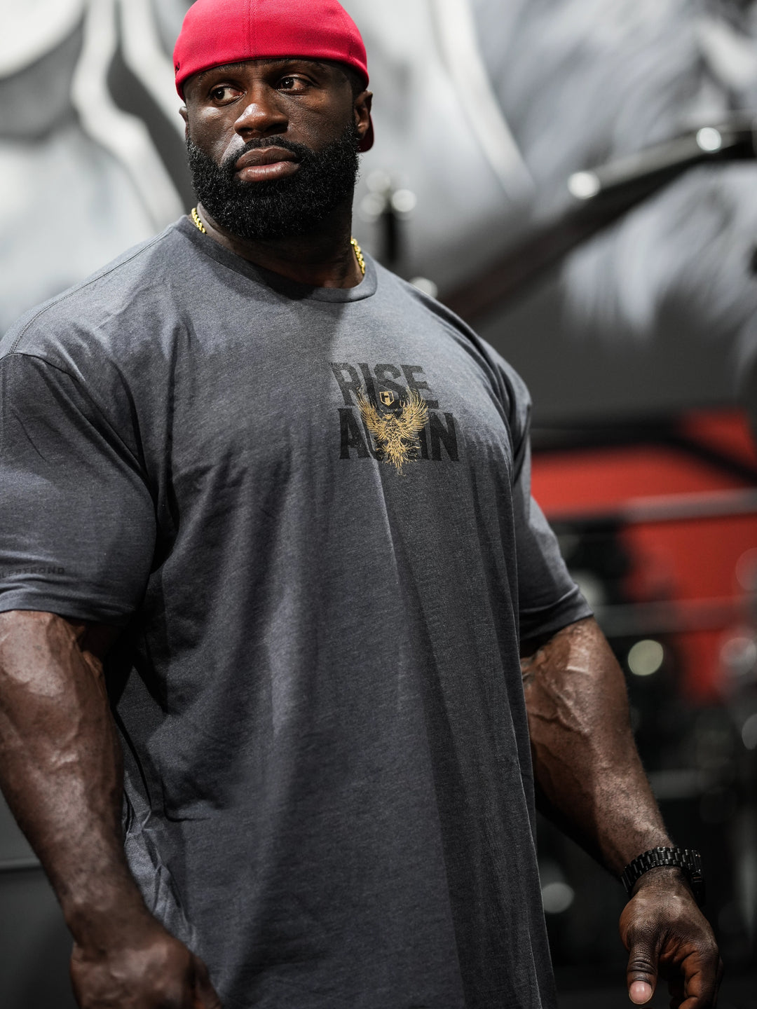 Samson Dauda wearing a gray t-shirt with text and a red cap, standing in front of a blurred background#color_charcoal