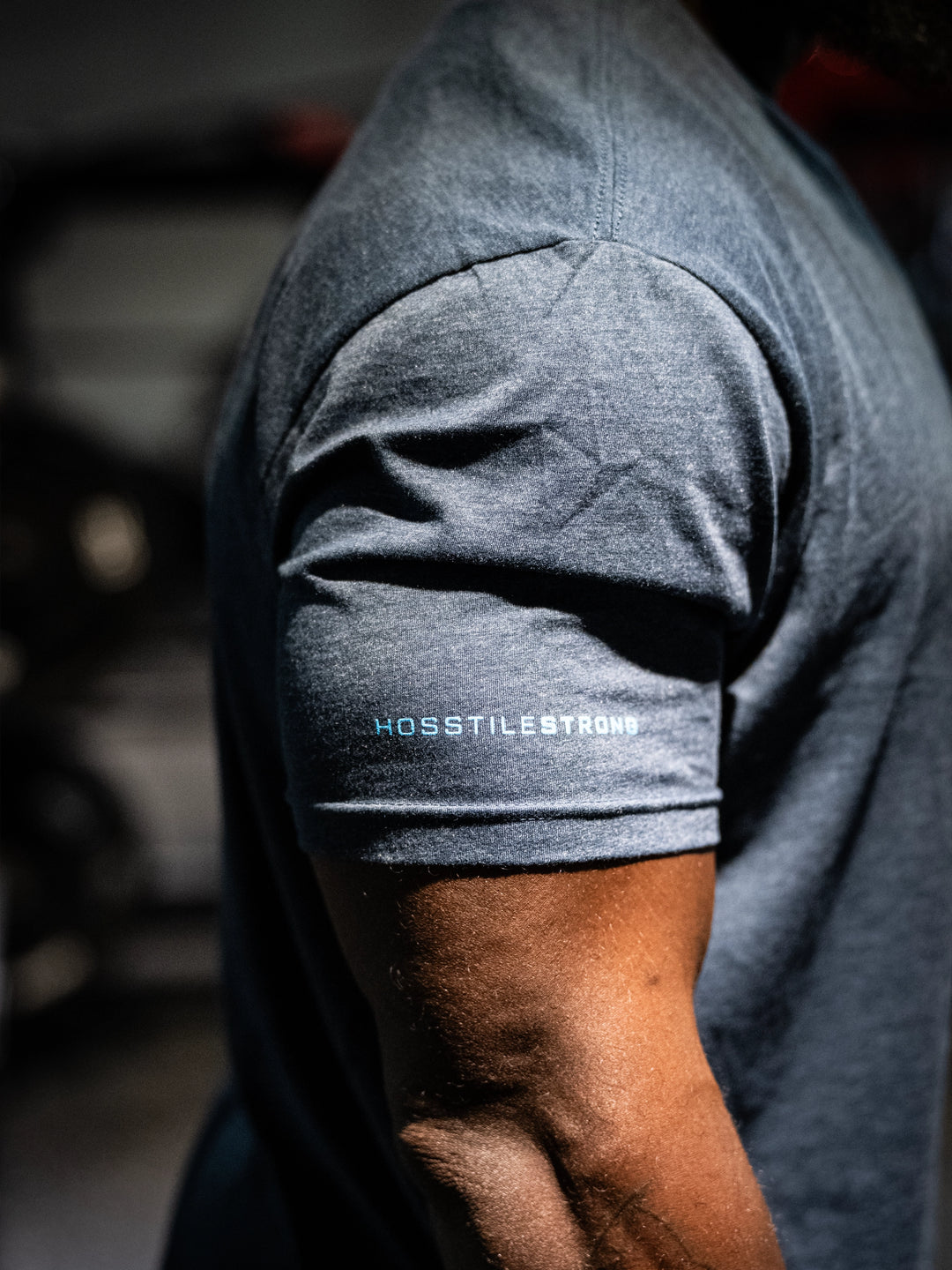 Navy t-shirt with 'Hosstile Strong' logo on sleeve, blurred background#color_navy