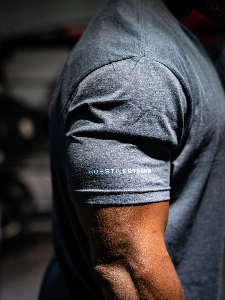 Navy t-shirt with 'Hosstile Strong' logo on sleeve, blurred background#color_navy