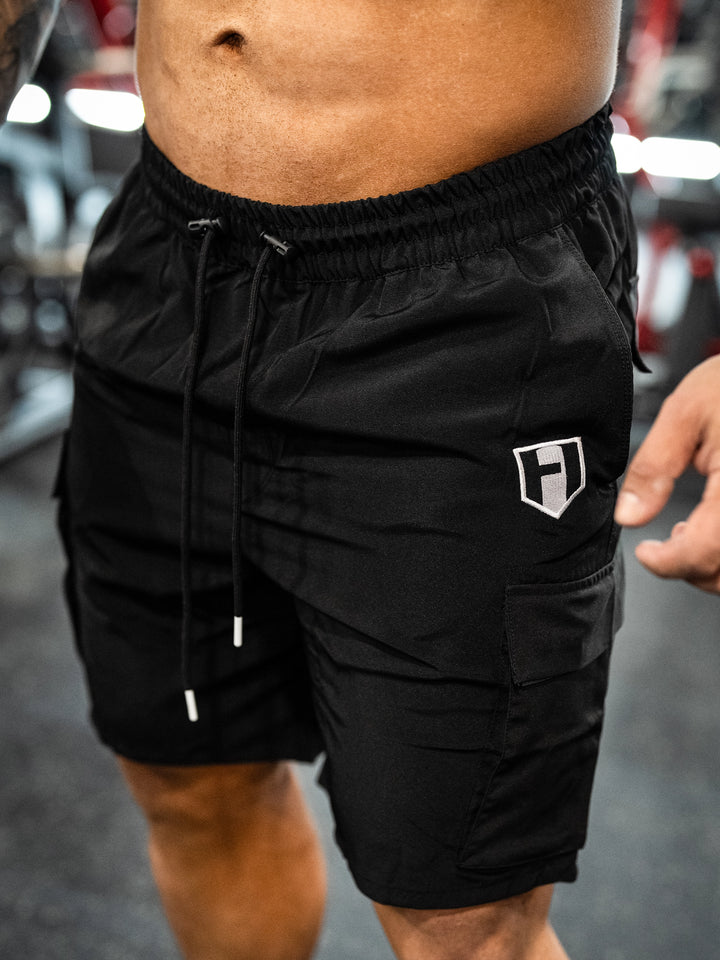 Bodybuilder wearing Shield Cargo Shorts#color_black
