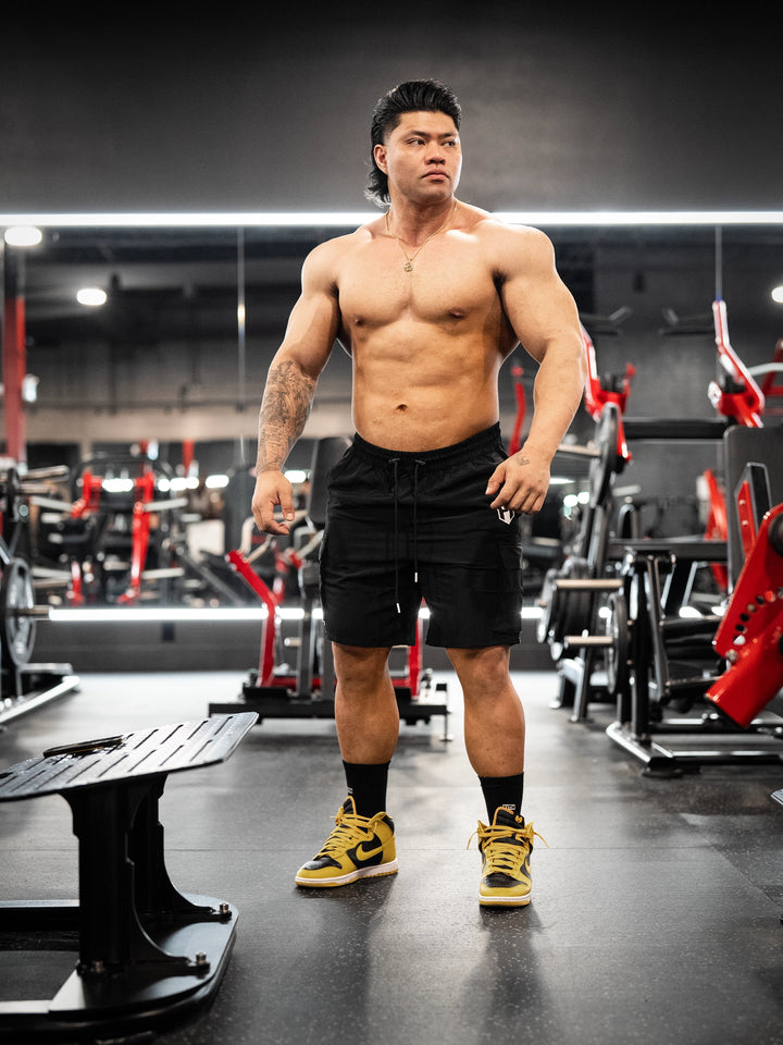 Bodybuilder wearing Shield Cargo Shorts#color_black