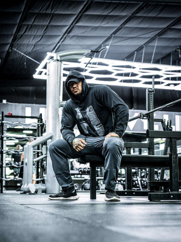 Bodybuilder Ben Chow wearing a black hoodie and cap in a gym setting#color_black