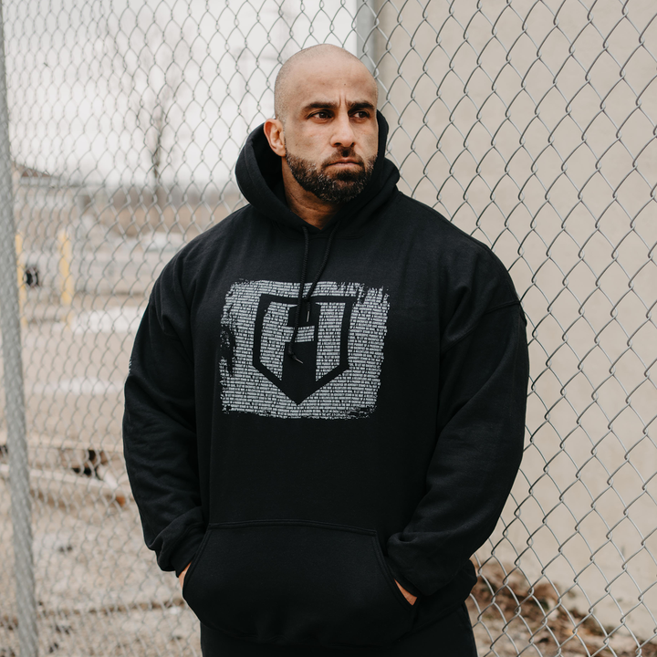 Bodybuilder Fouad Abiad standign in front of a fence wearing a Dark Knight hoodie 