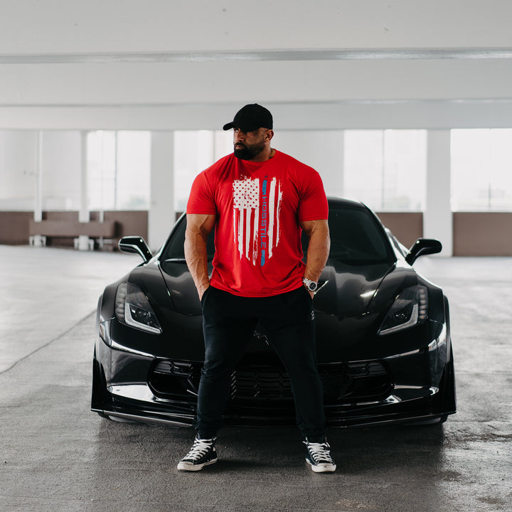 Bodybuilder Fouad Abiad standing in front of corvette wearing Patriot t-shirt